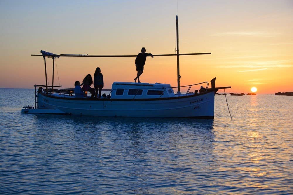 Navegación al ocaso frente a los acantilados de Formentera en barco clásico.